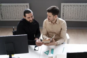 Two developers discussing project plans at a modern workspace, symbolizing collaboration and innovation offered by a React.js Vibe Coding Agency in 2025.