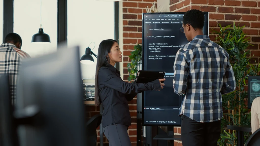 Team discussing code on a large screen in a modern office, representing Node.js AI-Powered Software Development outsourcing workflow.