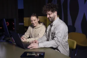 Two professionals collaborating on a laptop in a modern workspace, representing the Guide to Vibe Coding with React.js for executive decision-makers.